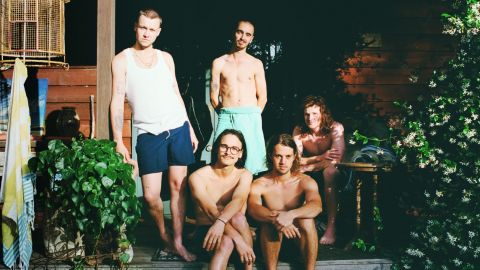A group of shirtless young men gather on a porch.