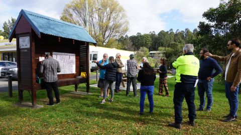 People stand around an outdoor noticeboard.