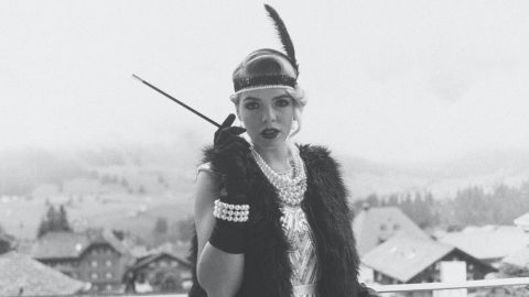 A woman dressed like a 1920s flapper looks at the camera. Image is black and white.