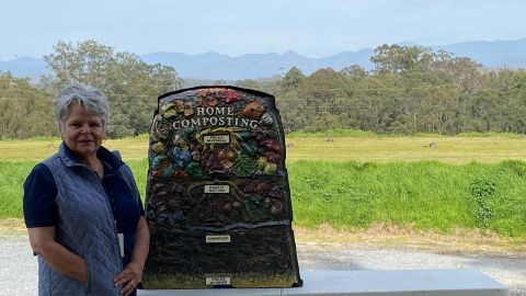 Workshop facilitator stands in front of a compost display mound