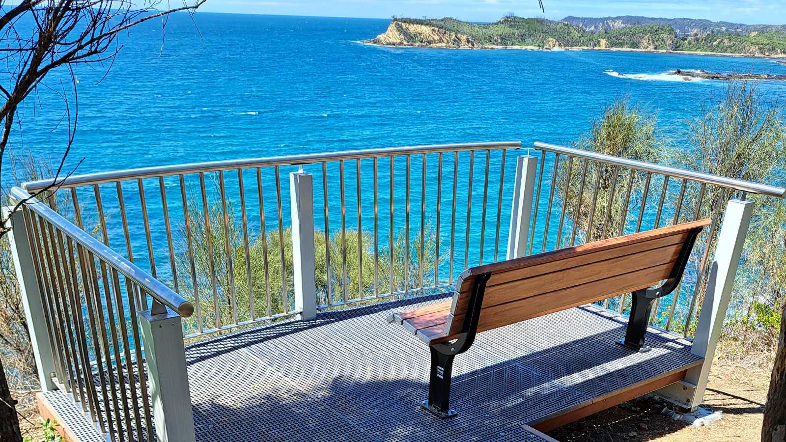 Image A viewing platform with a wooden bench seat overlooks blue ocean and a rugged coastline.