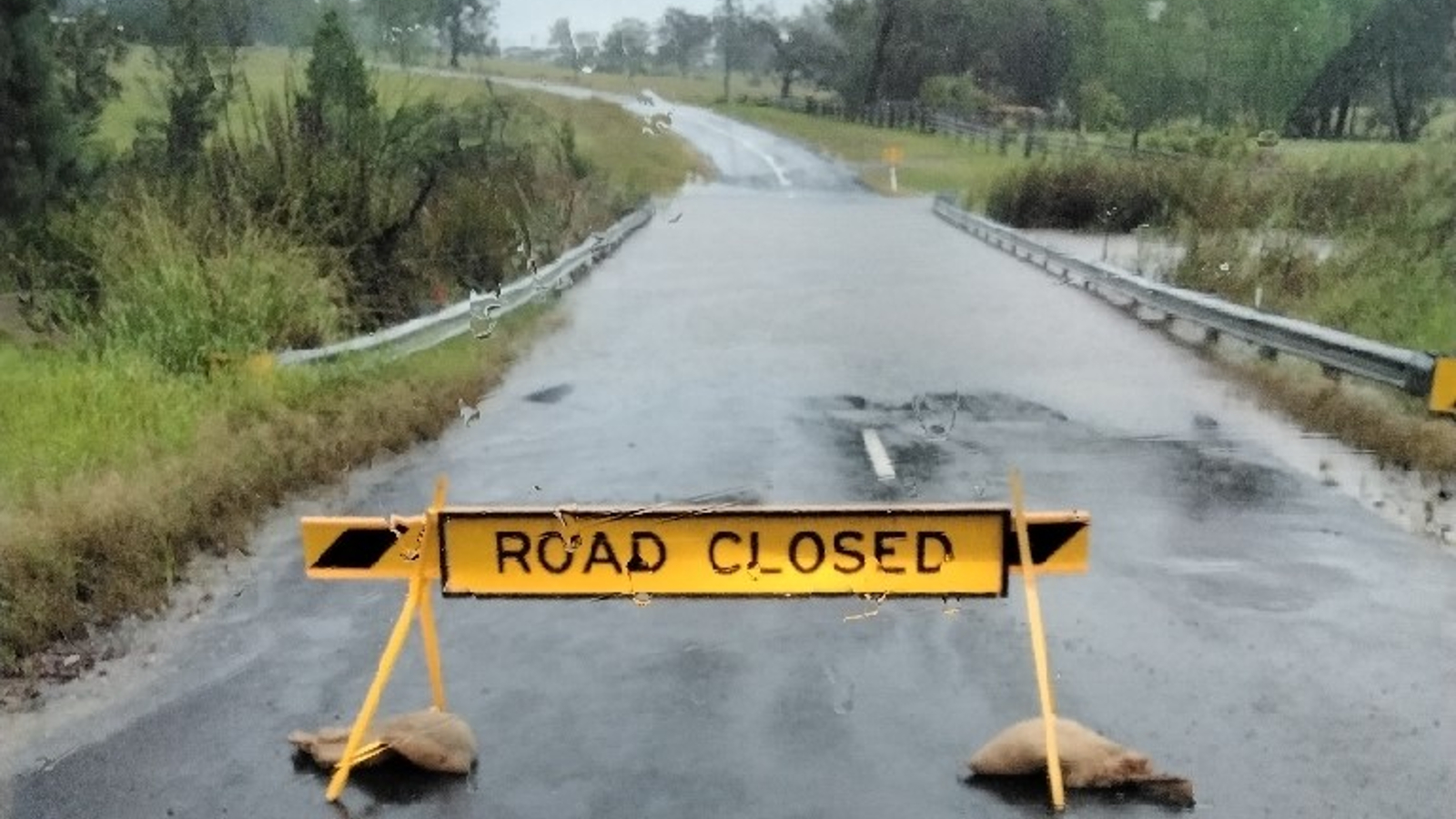 A road closed sign is sits in front of a flooded section of low-lying road.t before 