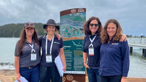 four women standing in front of a sign on a foreshore