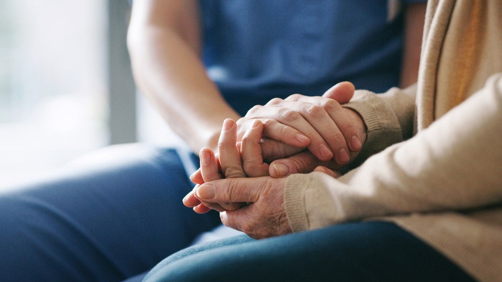 Two people seated holding hands in a supportive manner. banner image