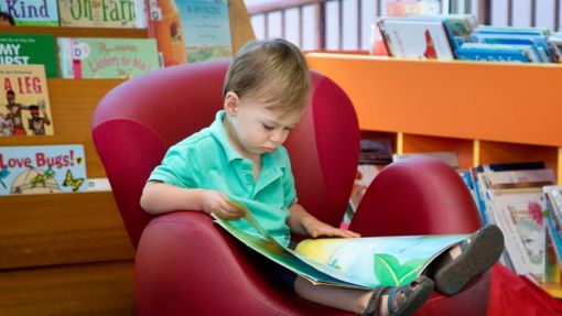 Young boy in a red chair reading a book.