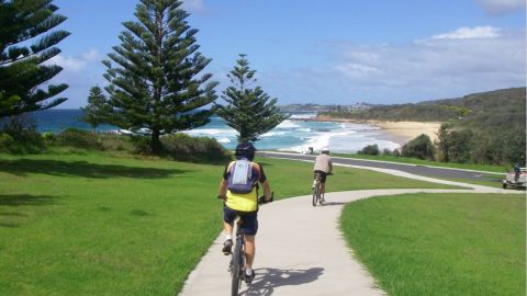 People riding a bike on a path with beach in background.