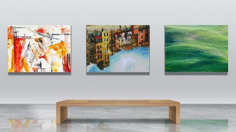 Three paintings hanging on a wall with a viewing bench in front of them.