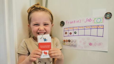 A smilimg child holds up cards next to a jobs chart.