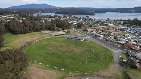 An aerial view of an oval with houses and Wagonga Inlet in the background