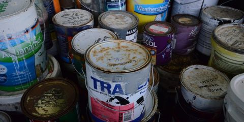 Cans of old used paint in a giant skip.