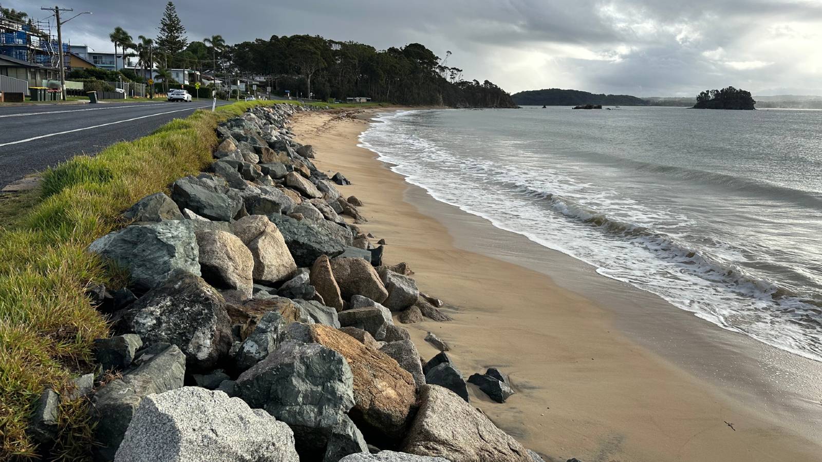 A rock seawall between the beach and road.