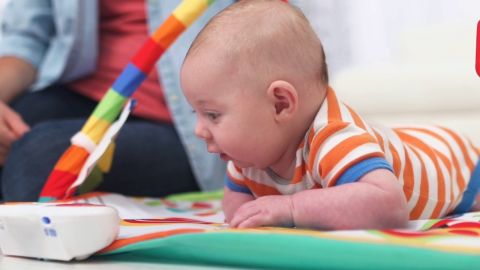 Baby lying on their tummy looking excited with play tools.