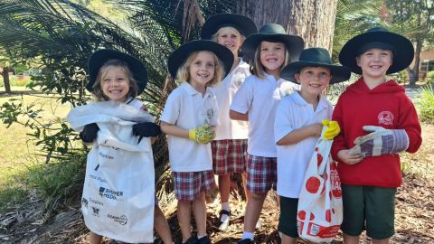 A cute group of kindy kids stand outside with clean-up bags and gloves.