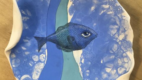 Detail of a blue fish painted onto a ceramic plate.
