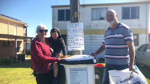 woman, child and man in front of large white garbage bin