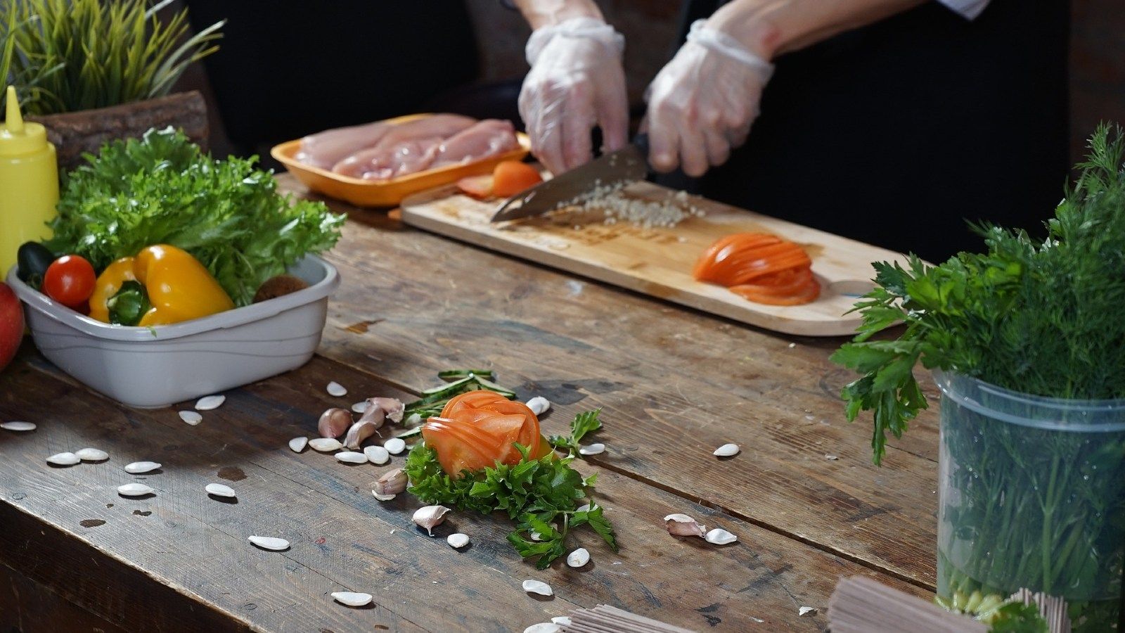 A woman's gloved hands chopping food with vegetables on a chopping board banner image