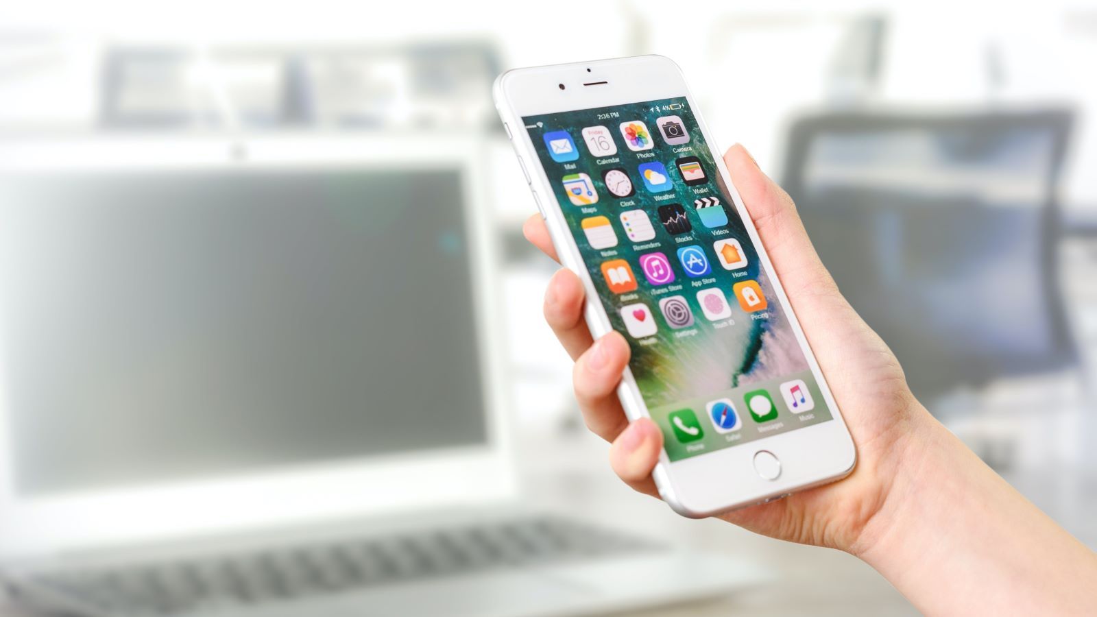 A person's hand holding a mobile phone in front of a computer screen banner image