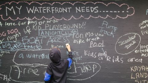 A young person writes on a blackboard with the heading 