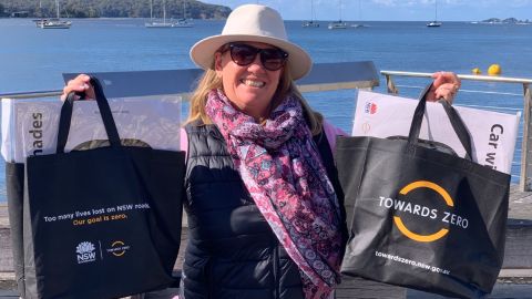 A lady holds up black show bags with 'Towards Zero' branding and NSW Government logos.