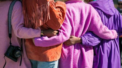 Cropped image of four women in bright coats with the arms about each other's waist.