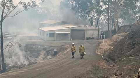 Two men in high vis walking in front of burnt shed surrounded by burnt forest