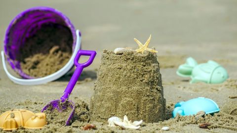 Bucket and spade and assorted moulds lying on the sand next to a sandcastle.