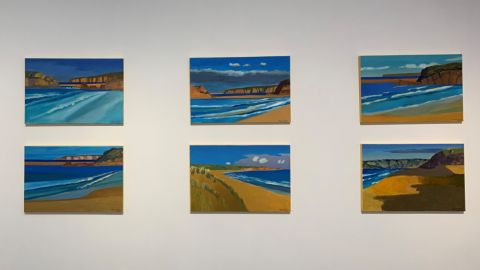 A series of six beach scene paintings on a wall.