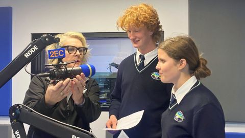 two teenagers in a recording studio with the producer adjusting the microphone.