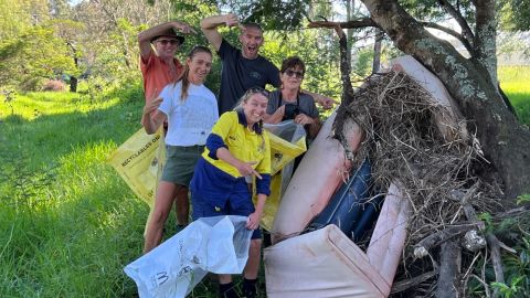 A group of people with clean up bags point to a discarded couch that has been washed in floods onto a tree.