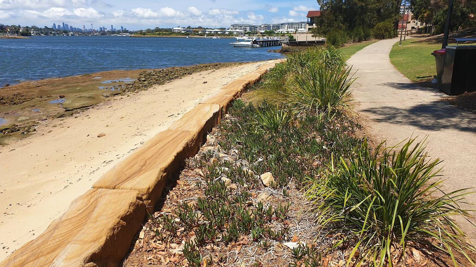 Image A sandstone seawall follws the edge of a strip of vegetation and a footpath