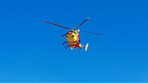 Red and yellow helicopter flies in a blue sky.