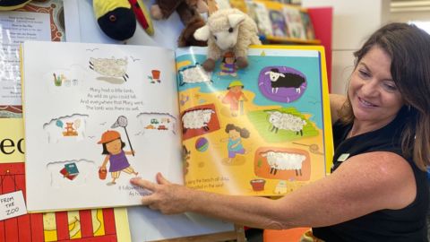 A teacher reading a toddlers story book in the library.