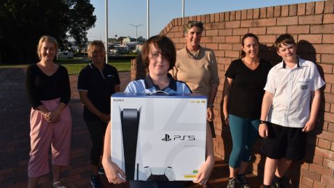 Six people stand in a group, with a boy at the front holding a PS5 box.