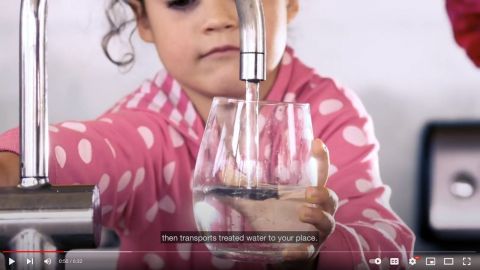 A screenshot from a video of a girl filling a glass with water from a tap.