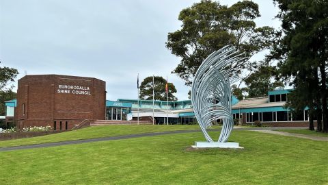 Large steel sculpture with lots of fronds on green lawn in front of dull brick building